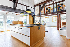 Offene Wohnküche im Fachwerkhaus mit Küchenblock, sichtbaren Balken und Galerie im Hintergrund