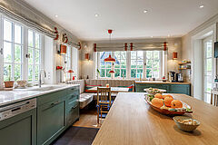 Landhausküche in Salbeigrün, Hamburg Altona | maßgefertigt von der Möbeltischlerei woodendesign – Blick über die Kücheninsel zur hellen Essecke mit Sitzbank