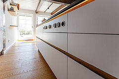 Kücheninsel im Fachwerkhaus mit weißen Fronten (inkl. BORA Knebelknöpfen) und Eichenakzent, Blick Richtung Terrassentür