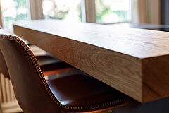 Detail der massiven Eiche-Theke – Nahaufnahme der Sitzkante mit Barstuhl und weichem Tageslicht im Hintergrund.