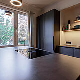 Einbauküche mit Sitztheke – Blick über die Inselarbeitsfläche zur Spülenzeile, hohen Schrankfronten und beleuchteten Wandregalen.