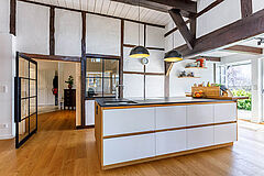 Küchenblock in Weiß und Holz vor Fachwerkwand, offene Wohnküche mit sichtbaren Deckenbalken