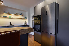 Hochschrankbereich der Einbauküche – großer Kühl-/Gefrierschrank neben Gerätehochschrank, Inselkante im Vordergrund.