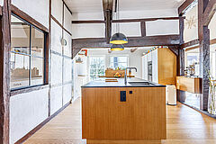 Moderne Kücheninsel aus Eiche mit dunkler Arbeitsplatte im offenen Fachwerkhaus, schwarze Pendelleuchten und sichtbare Balken.