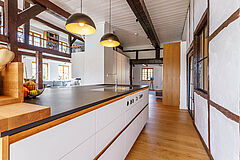 Blick entlang der Arbeitsplatte mit Spüle, Pendelleuchten und Fachwerkwand in der offenen Wohnküche