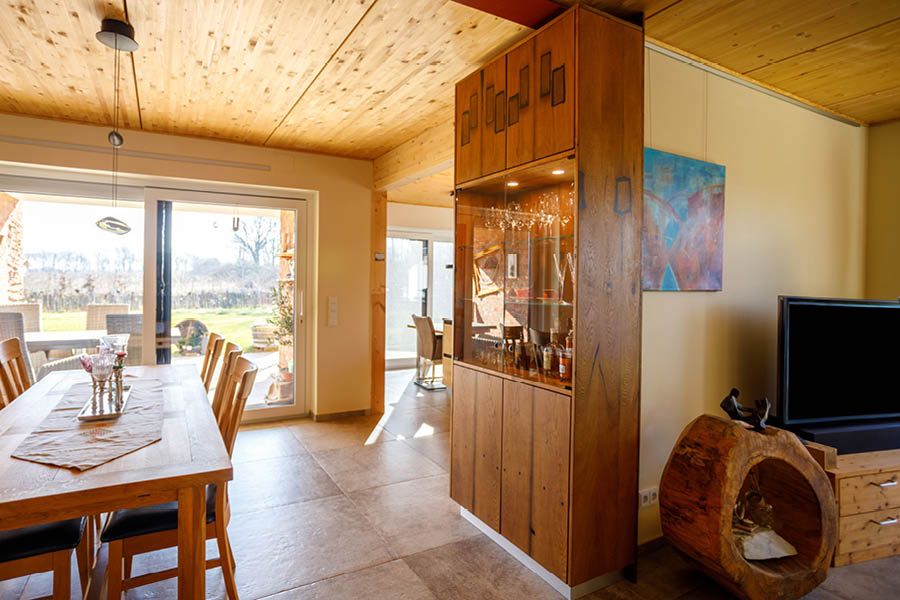 Raumteiler-Schrankwand mit Vitrine aus Massivholz zwischen Essen und Wohnen; beleuchtete Gläser, ruhige Frontaufteilung, luftiger Abschluss. Aktuelles – Trends – News im November 2025 | Möbeltischlerei woodendesign | Tischlerei Möbeltischler Möbelmanufaktur Hamburg