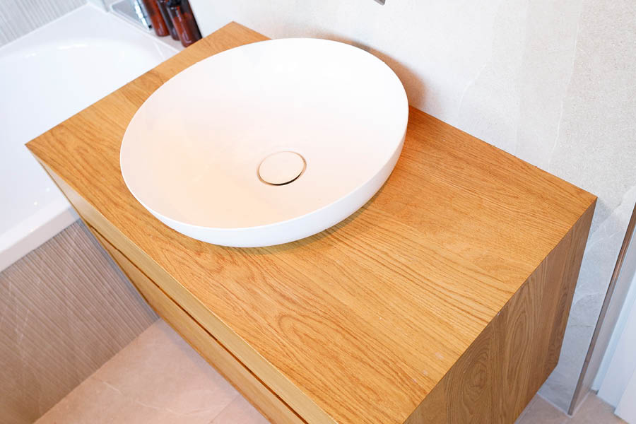 Eichen-Waschtischboard mit rundem, weißem Aufsatzwaschbecken; geölte Oberfläche, ruhiges Holzbild, sanfter Kontrast zu hellen Fliesen. Holz im Badezimmer | Aktuelles – Trends – News im Dezember 2025 | Möbeltischlerei Tischlerei Möbeltischler Möbelmanufaktur Hamburg