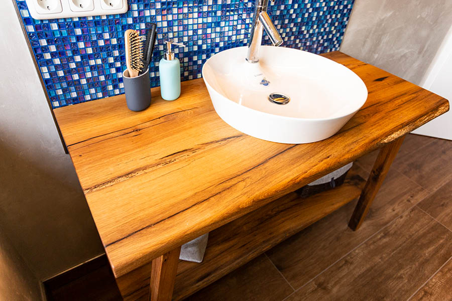 Waschtischkonsole aus Altholz mit rundem Aufsatzwaschbecken; geölte Oberfläche, offenes Ablagefach, blaue Mosaikfliesen als Rückwand. Holz im Badezimmer | Aktuelles – Trends – News im Dezember 2025 | Möbeltischlerei Tischlerei Möbeltischler Möbelmanufaktur Hamburg
