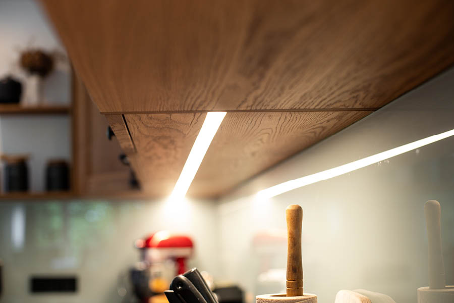 Detailaufnahme einer LED-Unterbauleuchte unter Holzregal für gezielte Beleuchtung der Arbeitsfläche – Lichtplanung Küche | Aktuelles – Trends – News im April 2026 | Möbeltischlerei Tischlerei Möbeltischler Möbelmanufaktur Hamburg
