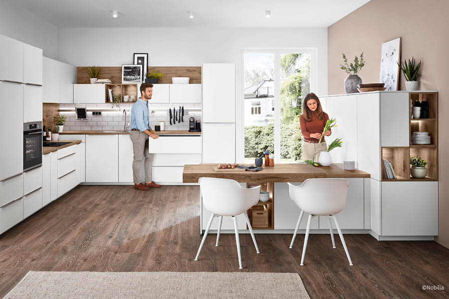 Offene weiße Küche mit angesetztem Holztisch und zwei Stühlen als integrierter Essplatz | Sitzplätze Küche | Aktuelles – Trends – News im August 2026 | Möbeltischlerei Tischlerei Möbeltischler Möbelmanufaktur Hamburg