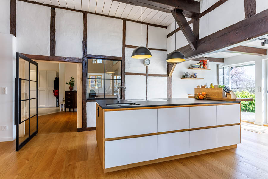 Küchenblock in Weiß und Holz vor Fachwerkwand, offene Wohnküche mit sichtbaren Deckenbalken