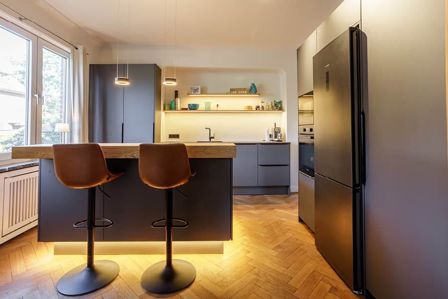 Einbauküche mit Sitztheke in Hamburg-Bergedorf – Kücheninsel mit zwei Barstühlen, Sockelbeleuchtung, Spülenzeile und hohe Schrankfronten.